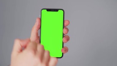 Gri arka planda yeşil ekranlı akıllı telefon kullanan erkek eller. Krom anahtar