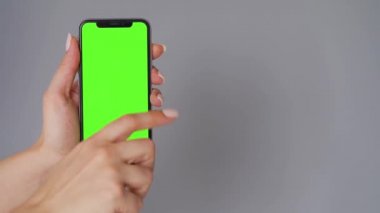 Gri arka planda yeşil ekranlı akıllı telefon kullanan kadın eller. Krom anahtar.