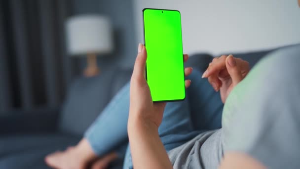 Kobieta w domu leży na kanapie i używa smartfona z zielonym ekranem makiety w trybie pionowym. Dziewczyna przeglądająca Internet, oglądająca treści, filmy, blogi. POV. — Wideo stockowe