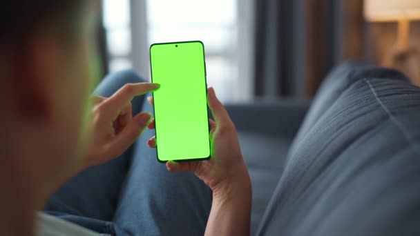 Vrouw thuis liggend op een bank en met behulp van smartphone met groene mock-up scherm in verticale modus. Meisje surfen op internet, kijken naar inhoud, video 's, blogs. POV. — Stockvideo