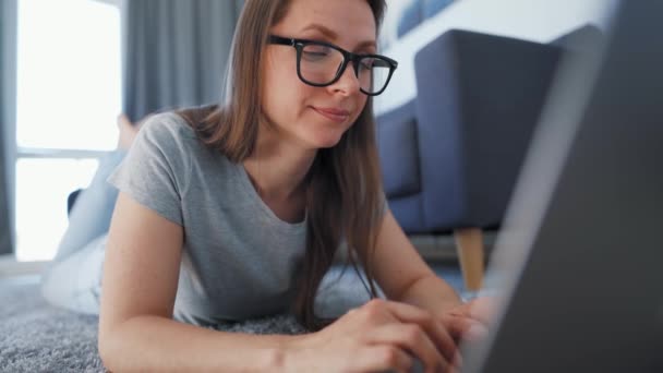 La mujer está tirada en el suelo y trabajando en un portátil. Concepto de trabajo remoto. — Vídeo de stock