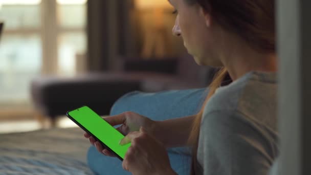 Femme à la maison couchée sur un canapé et utilisant un smartphone avec écran vert maquette en mode vertical. Fille naviguant sur Internet, regarder du contenu, vidéos, blogs. Point de vue. — Video