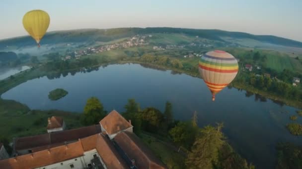 Barevné horkovzdušné balóny létají nad středověkým hradem a jezerem v ranní mlze. Manévrovatelné letové a energetické smyčky. Cestování, dobrodružství, festival. — Stock video