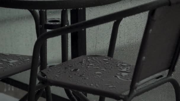 Lluvia fuerte vierte los muebles en el balcón o terraza. Las gotas caen por el cristal de la valla — Vídeo de stock