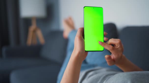 Evde bir kadın kanepeye uzanıyor ve dikey modda yeşil ekran ile akıllı telefon kullanıyor. İnternette gezinen, içerik izleyen, videolar, bloglar. POV. — Stok video