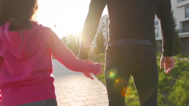 Папа и дочь прогуливаются по их району на закате. Ребенок держит отцов за руку. Медленное движение — стоковое видео