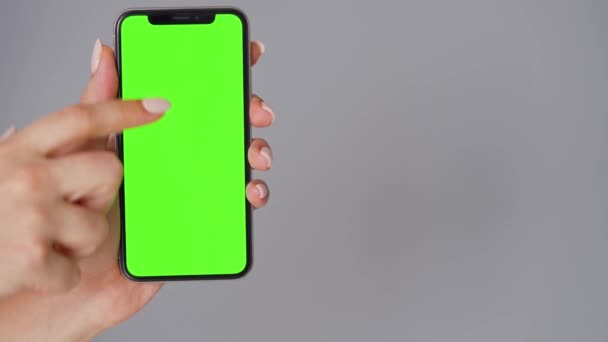 Manos femeninas usando un smartphone con una pantalla verde sobre un fondo gris. Clave de croma. — Vídeos de Stock