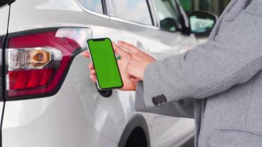 Kadın, bir arabaya yakıt ikmali için akıllı telefondan mobil uygulama kullanıyor. Yeşil ekranlı akıllı telefon. Krom anahtar