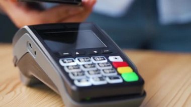Akıllı telefondan yapılan temassız ödeme. Kablosuz ödeme konsepti. Yakın plan, kadın banka terminalindeki siparişi ödemek için akıllı telefon nakitsiz cüzdan teknolojisi kullanıyor..