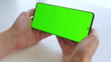 Yatay modda yeşil ekranlı akıllı telefon kullanan kadın eller. Krom anahtar.