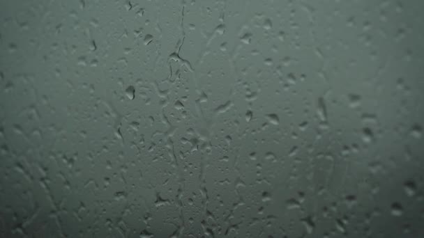 Κοντινό πλάνο ενός ποτηριού με σταγόνες νερού ενώ έξω βρέχει. Σταγόνες βροχής μέσα από γυαλί. — Αρχείο Βίντεο