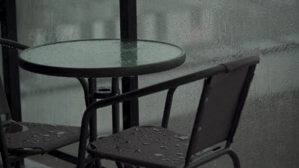 Zware regenval giet het meubilair naar beneden op het balkon of terras. druppels lopen door het glas van het hek — Stockvideo
