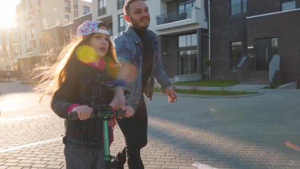 Papá le está enseñando a su hija a montar un scooter al atardecer. — Vídeos de Stock