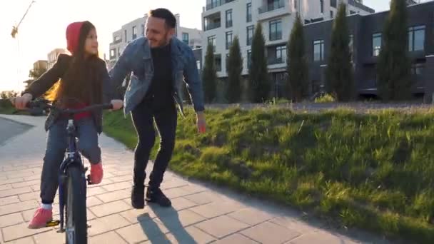 Papá le está enseñando a su hija a andar en bicicleta al atardecer — Vídeos de Stock