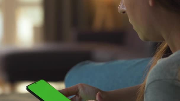 Женщина дома лежит на диване и использует смартфон с зеленым макетом экрана в вертикальном режиме. Девочки просматривают Интернет, смотрят контент, видео, блоги. — стоковое видео