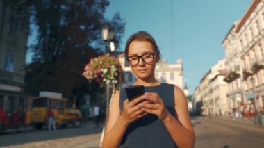Eski bir caddede yürüyen ve günbatımında akıllı telefon kullanan bir kadın.