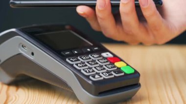 Akıllı telefondan yapılan temassız ödeme. Kablosuz ödeme konsepti. Yakın plan, kadın banka terminalindeki siparişi ödemek için akıllı telefon nakitsiz cüzdan teknolojisi kullanıyor..