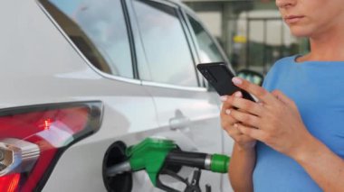 Arabası yakıt ikmali yaparken akıllı telefon kullanan bir kadın.