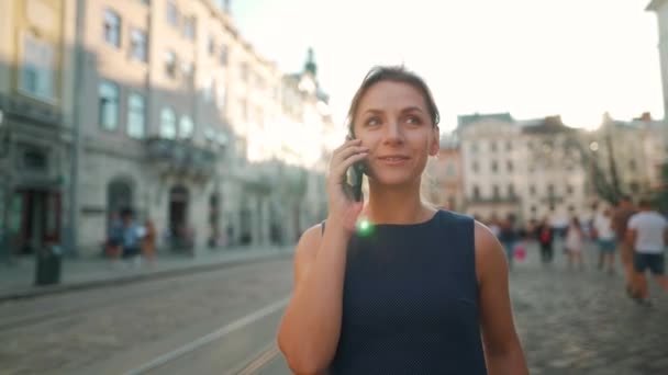 Frau steht auf dem alten Platz und spricht mit Smartphone. Im Hintergrund fährt eine gelbe Straßenbahn vorbei. Warmer Sommerabend — Stockvideo