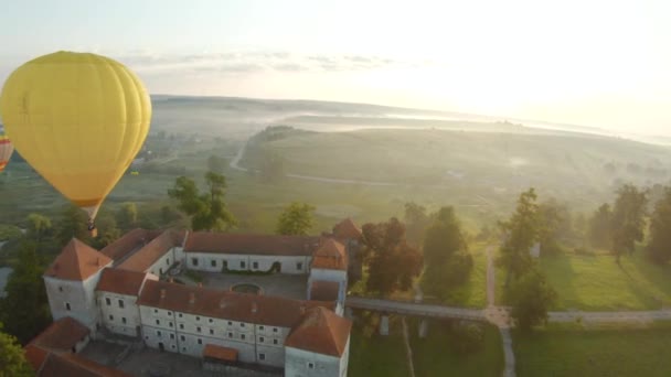 Barevné horkovzdušné balóny létají nad středověkým hradem a jezerem v ranní mlze. Manévrovatelný let. Cestování, dobrodružství, festival. — Stock video