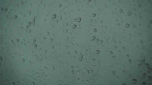 Κοντινό πλάνο ενός ποτηριού με σταγόνες νερού ενώ έξω βρέχει. Σταγόνες βροχής μέσα από γυαλί. — Αρχείο Βίντεο