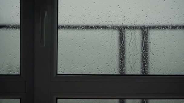 Buiten regent het en binnen zicht op het raamkozijn en glas. Sluiten van een glas met waterdruppels terwijl het buiten regent. Druppels regen door glas. — Stockvideo