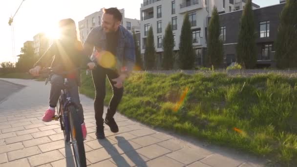 O pai está a ensinar a filha a andar de bicicleta ao pôr-do-sol. Movimento lento — Vídeo de Stock