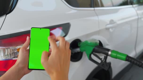 Mulher usa um aplicativo móvel em um smartphone para pagar para reabastecer um carro. Smartphone com uma tela verde. Chave Chroma — Vídeo de Stock