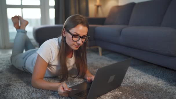 Kobieta leży na podłodze i dokonuje zakupu online za pomocą karty kredytowej i laptopa. Zakupy online, technologia stylu życia — Wideo stockowe