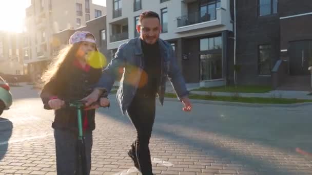 Dad is teaching daughter how to ride a scooter at sunset — Stock Video