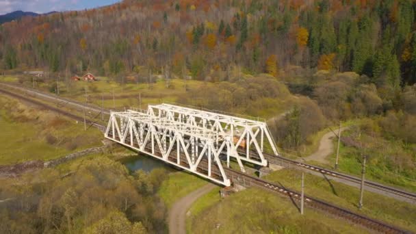 Vue de la hauteur sur le paysage montagneux d'automne forêt jaune, rivière, pont ferroviaire et véhicule qui passe dessus — Video