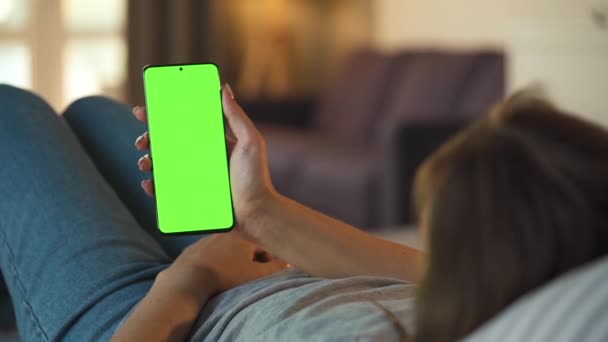 Frau zu Hause auf dem Sofa liegend und Smartphone mit grünem Bildschirm im vertikalen Modus. Mädchen surfen im Internet, schauen Inhalte, Videos, Blogs. — Stockvideo