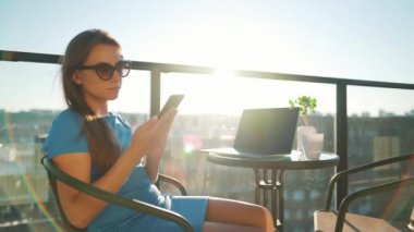Kadın gün batımının arka planına karşı balkonda çalışıyor. Uzak çalışma konsepti