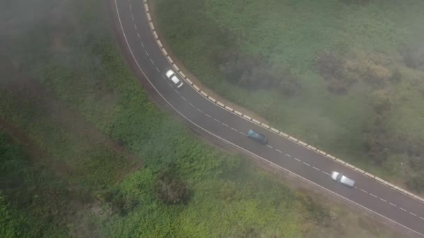 Vliegend door de wolken over een bergweg omringd door groene vegetatie. Verkeer op de weg — Stockvideo