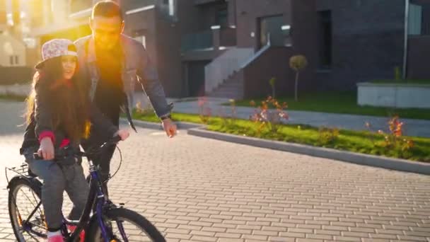 Papá le está enseñando a su hija a andar en bicicleta al atardecer. Movimiento lento — Vídeos de Stock