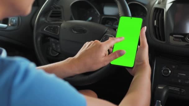 여성 운전자가 차 안에서 스마트폰을 사용하고 있습니다. 녹색 화면을 가진 크로마키 스마트폰입니다. 자동 항법 장치. 인터넷 중독 — 비디오