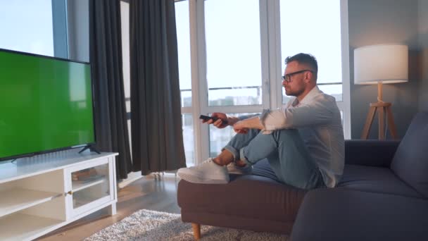 Man thuis liggend op een bank en tv aan het kijken met groen mock-up scherm — Stockvideo