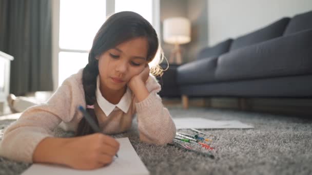 Söt koncentrerad flicka ritar med färgade pennor som ligger på golvet ensam — Stockvideo