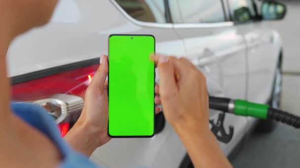 Mujer utiliza una aplicación móvil en un teléfono inteligente para pagar por repostar un coche. Smartphone con pantalla verde. Clave de croma — Vídeo de stock