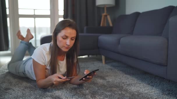 Mujer está tirada en el suelo y hace una compra en línea con una tarjeta de crédito y un teléfono inteligente. Compras en línea, tecnología de estilo de vida — Vídeos de Stock