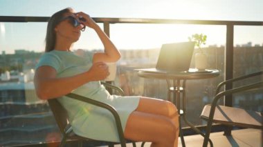 Kadın kahve içiyor ve güneş batarken balkonda dinleniyor. Uzak çalışma konsepti