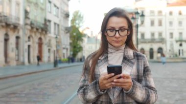 Eski bir caddede yürüyen ve akıllı telefon kullanan bir kadın.