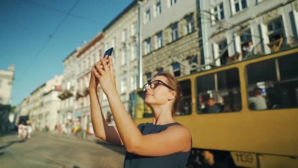 Mulher fica em uma rua velha e tira uma foto ou vídeo em um smartphone ao pôr do sol — Vídeo de Stock