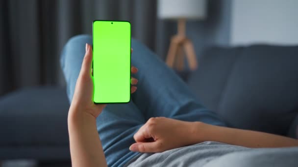 Vrouw thuis liggend op een bank en met behulp van smartphone met groene mock-up scherm in verticale modus. Meisje surfen op internet, kijken naar inhoud, video 's, blogs. POV. — Stockvideo