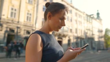Gözlüklü kadın eski bir sokakta duruyor ve akıllı telefon kullanıyor.