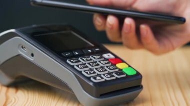 Akıllı telefondan yapılan temassız ödeme. Kablosuz ödeme konsepti. Yakın plan, kadın banka terminalindeki siparişi ödemek için akıllı telefon nakitsiz cüzdan teknolojisi kullanıyor..