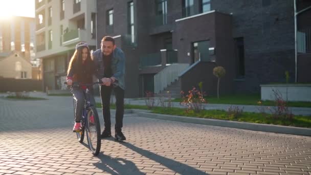 Papá le está enseñando a su hija a andar en bicicleta al atardecer. Movimiento lento — Vídeos de Stock