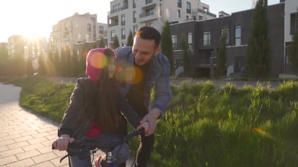 Dad is teaching daughter how to ride bicycle at sunset. Slow motion — Stock Video