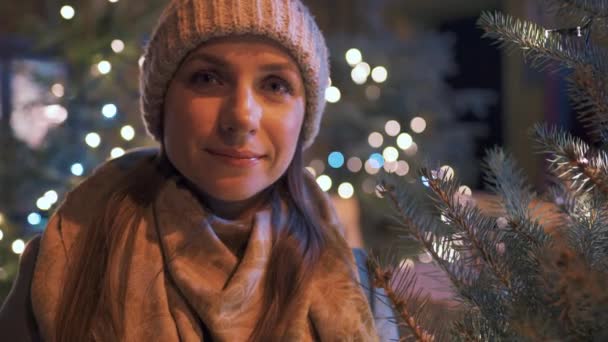 Mutlu bir kadının portresi Noel süslemelerinin arka planına karşı. Ellerini ovuyor, soğuktan koruyor. — Stok video