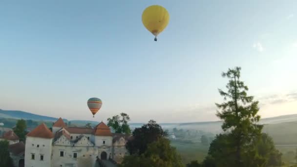 Barevné horkovzdušné balóny létají nad středověkým hradem a jezerem v ranní mlze. Manévrovatelný let. Cestování, dobrodružství, festival. — Stock video